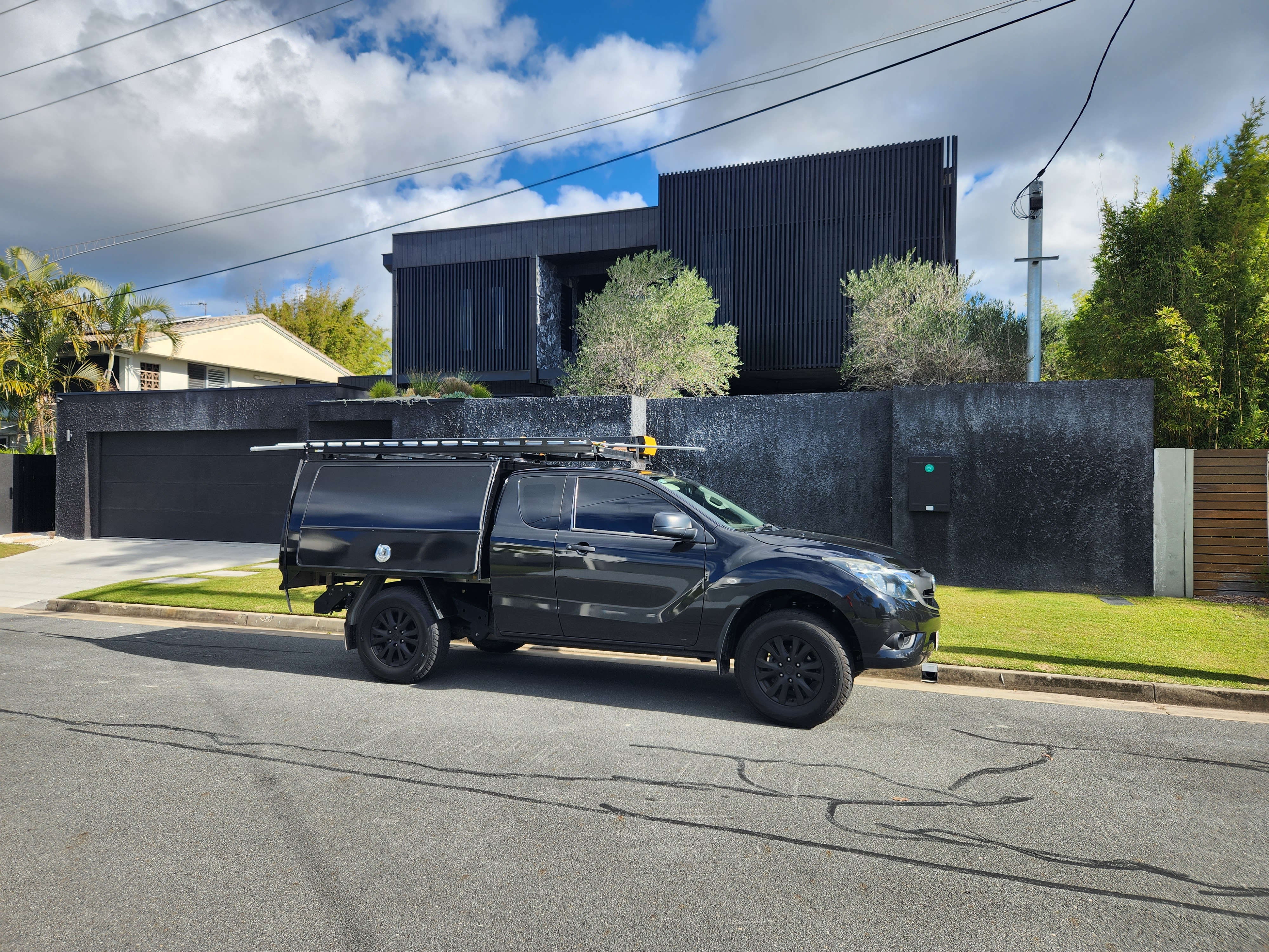 A black utility vehicle parked in front of a modern house with a dark exterior and landscaped yard, under a partly cloudy sky.